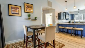 A dining area with a table and chairs, a kitchen with bar stools, and framed artwork on the wall.