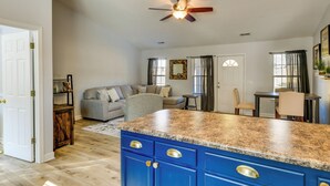 A spacious living area with a blue kitchen island, a grey sofa, and a dining table.