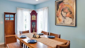 Une salle à manger avec une table en bois, des chaises, une horloge et un tableau accroché au mur.