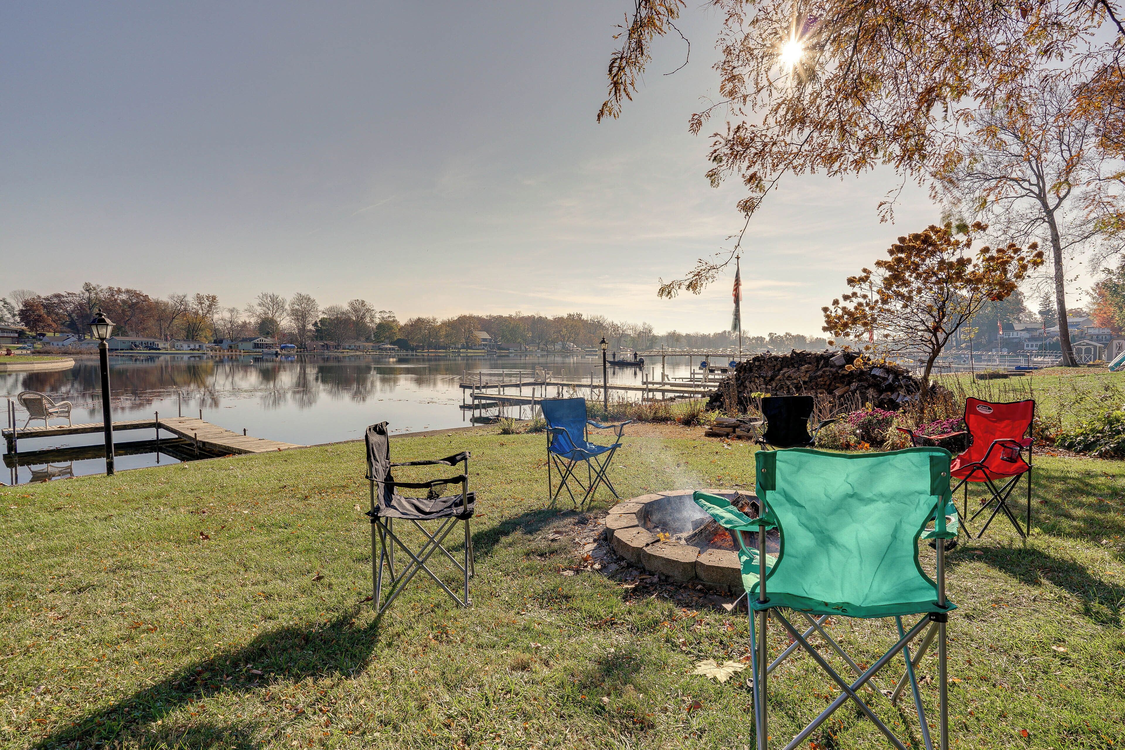 A lakeside setting with a dock, chairs, and a fire pit.