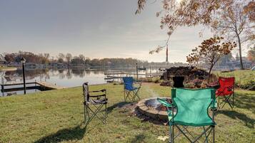 A lakeside setting with a dock, chairs, and a fire pit.