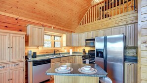 Cocina de cabaña de madera con una isla central, electrodomésticos de acero inoxidable y armarios de madera.