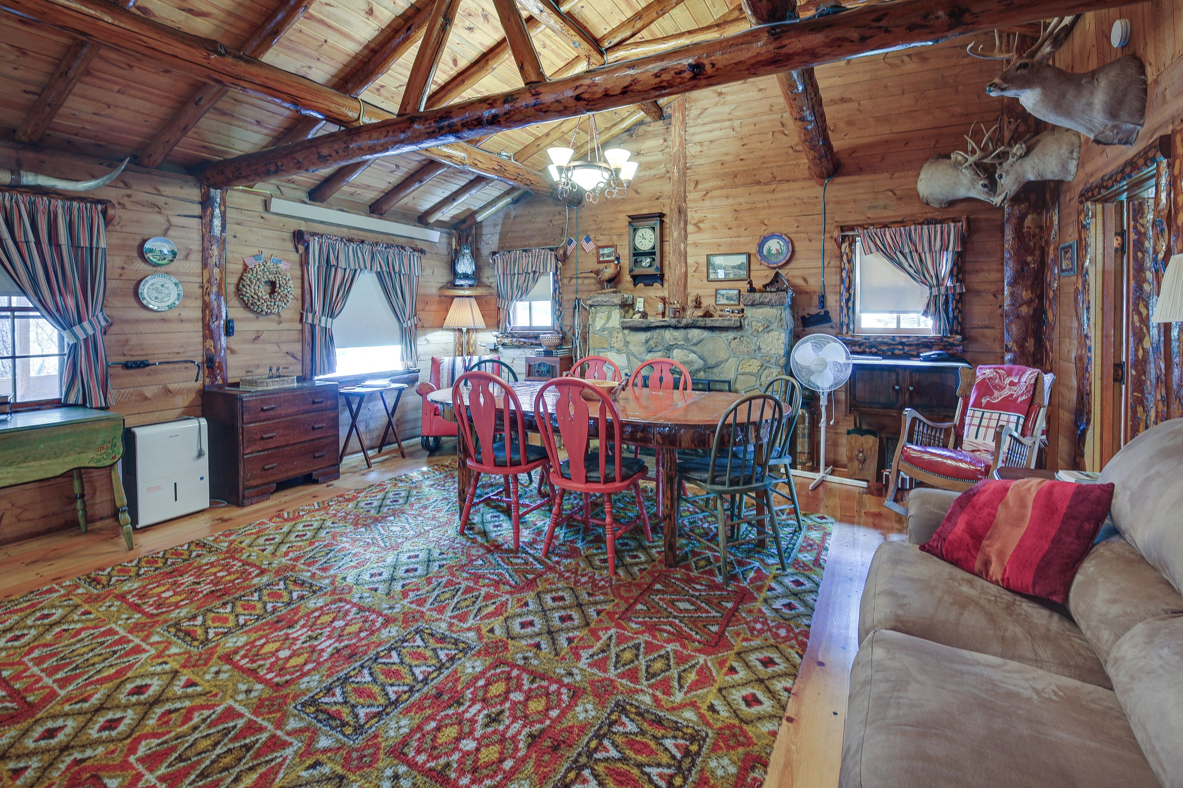 A rustic cabin interior with a wooden dining area, a stone fireplace, and a cozy living room with a couch.