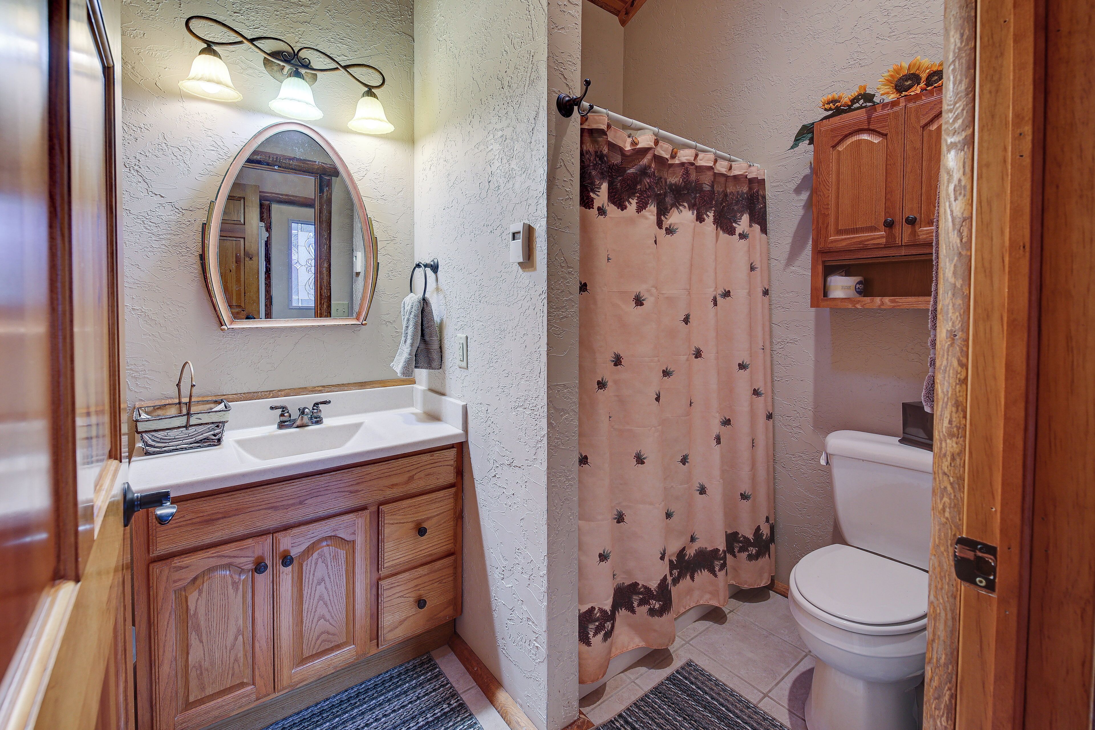 A bathroom with a wooden vanity, a sink, a mirror, a shower curtain with a floral pattern, and a toilet.