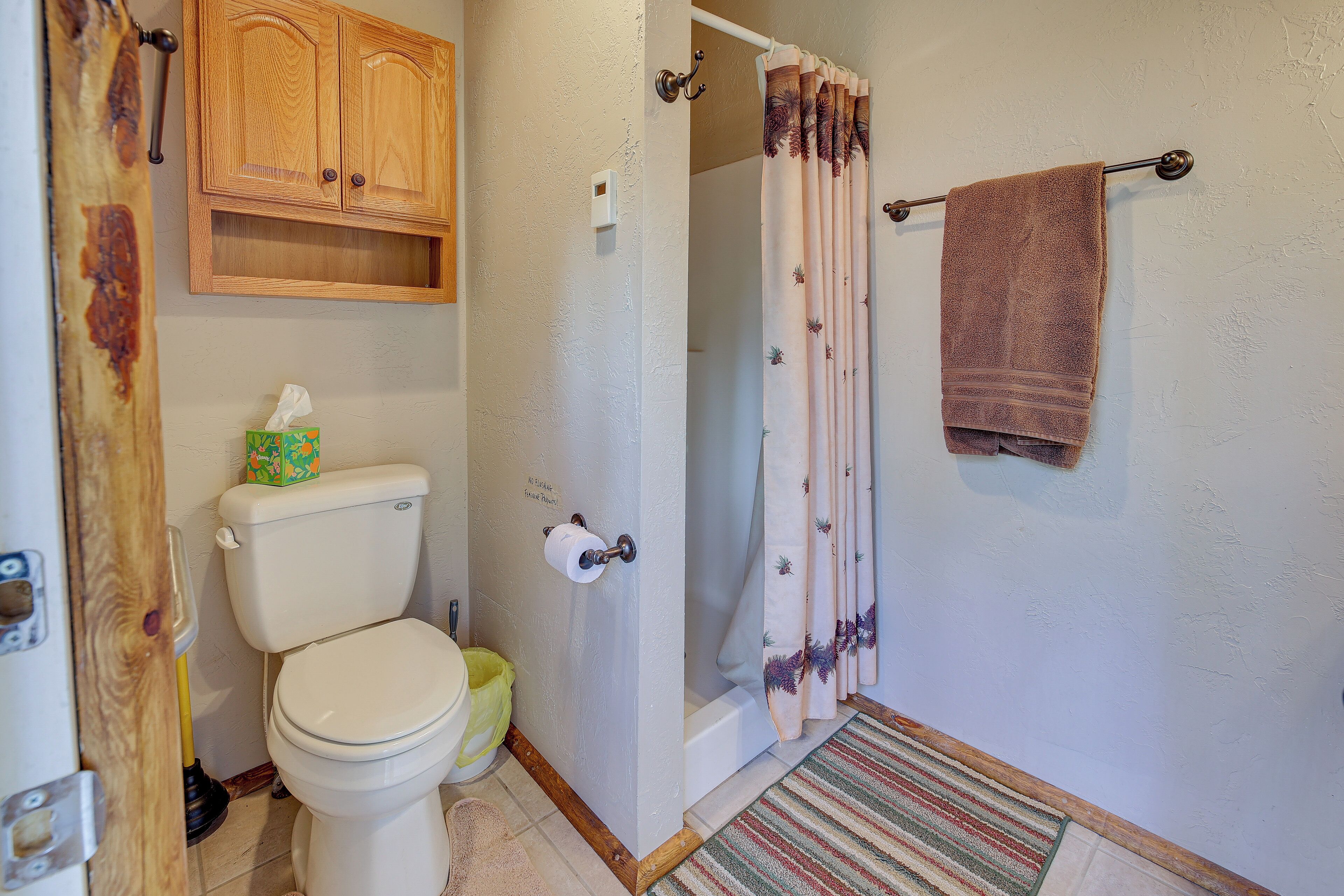 A bathroom with a toilet, a wooden cabinet, a shower curtain, and a towel rack.