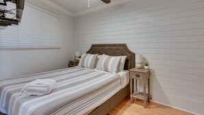Ein ordentlich bezogenes Bett mit Streifenmuster, ein gefaltetes Handtuch, ein Nachttisch mit Lampe und ein Deckenventilator.