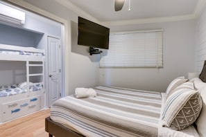 A bedroom with a bunk bed, a flat-screen TV, a window with blinds, and a bed with striped bedding.