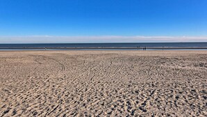 Ein weiter Sandstrand mit Fußabdrücken, die zum Wasser führen.