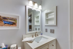 A bathroom with a white sink, three light fixtures above the mirror, and a framed picture of a blue boat on the wall.