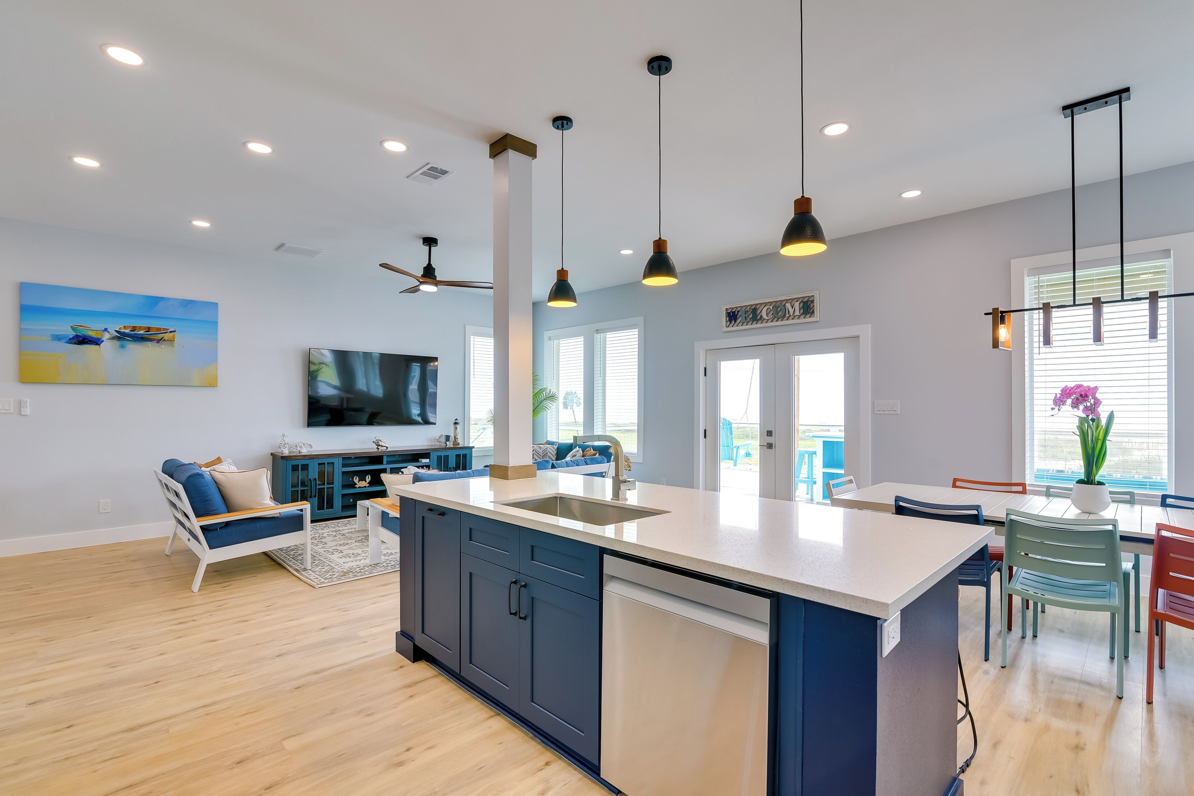 A modern kitchen with a central island, a dining area with chairs, and a living room with a sofa and TV.