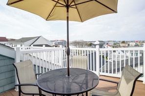 A balcony with a round table and two chairs, a white railing, and a view of a residential area. - Walk to Ocean City Beach: Condo w/ Rooftop Deck (Ocean City)