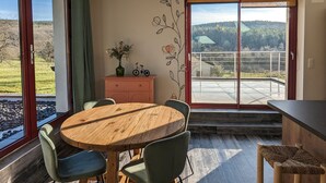 Un coin repas avec une table et des chaises en bois, une vue sur l’extérieur grâce à une porte-fenêtre coulissante et un ventilateur de plafond.