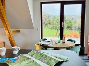 Ein Essbereich mit einem runden Tisch, Stühlen und Blick auf eine grüne Landschaft durch eine Glastür.