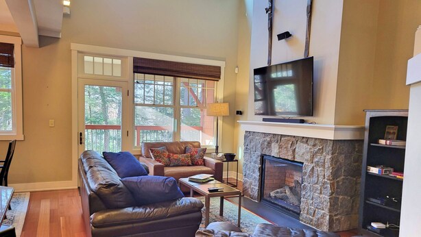 A spacious living room with a stone fireplace, leather sofas, a flat-screen TV, and a bookshelf. - Open plan, AC/FP, pool access, at South Peak, ski shuttle. P002F by LRS (Lincoln)