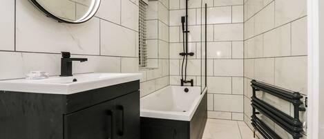 Un baño moderno con tocador negro, bañera blanca y sistema de ducha negro.