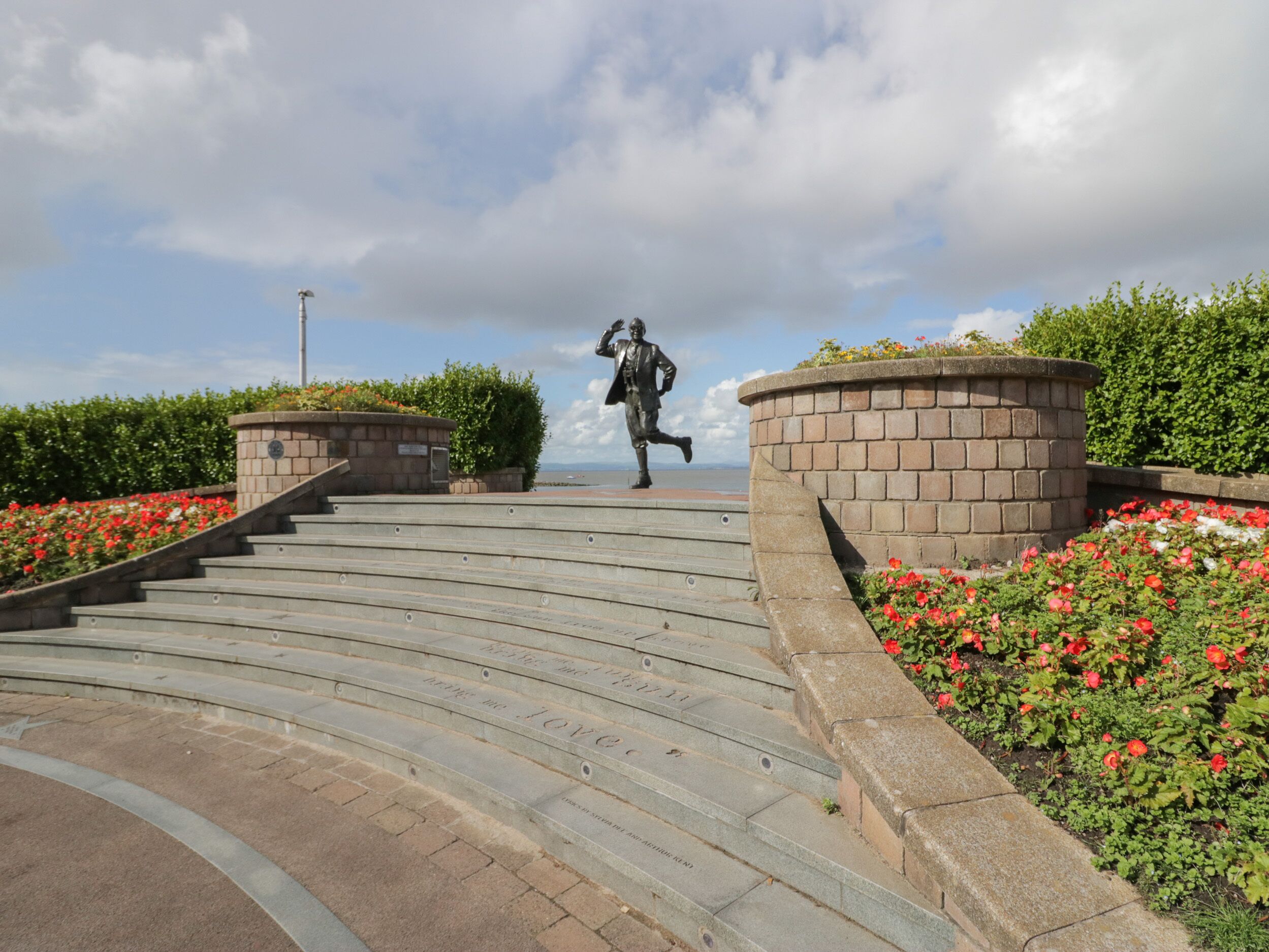 Eine Treppe führt zu einer Statue, umgeben von Ziegelmauern und roten Blumen.