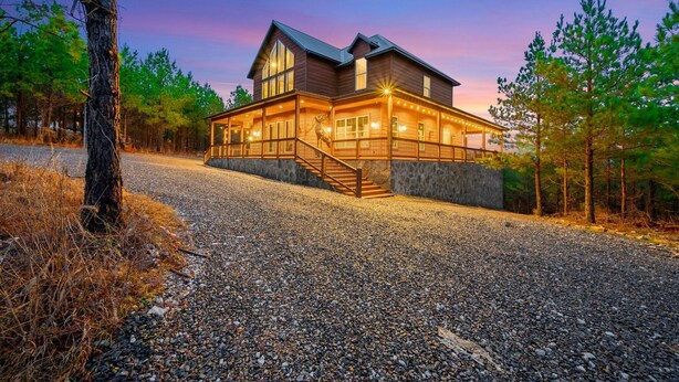 A large, two-story wooden house with a stone foundation, a covered porch, and a staircase leading to the main entrance.