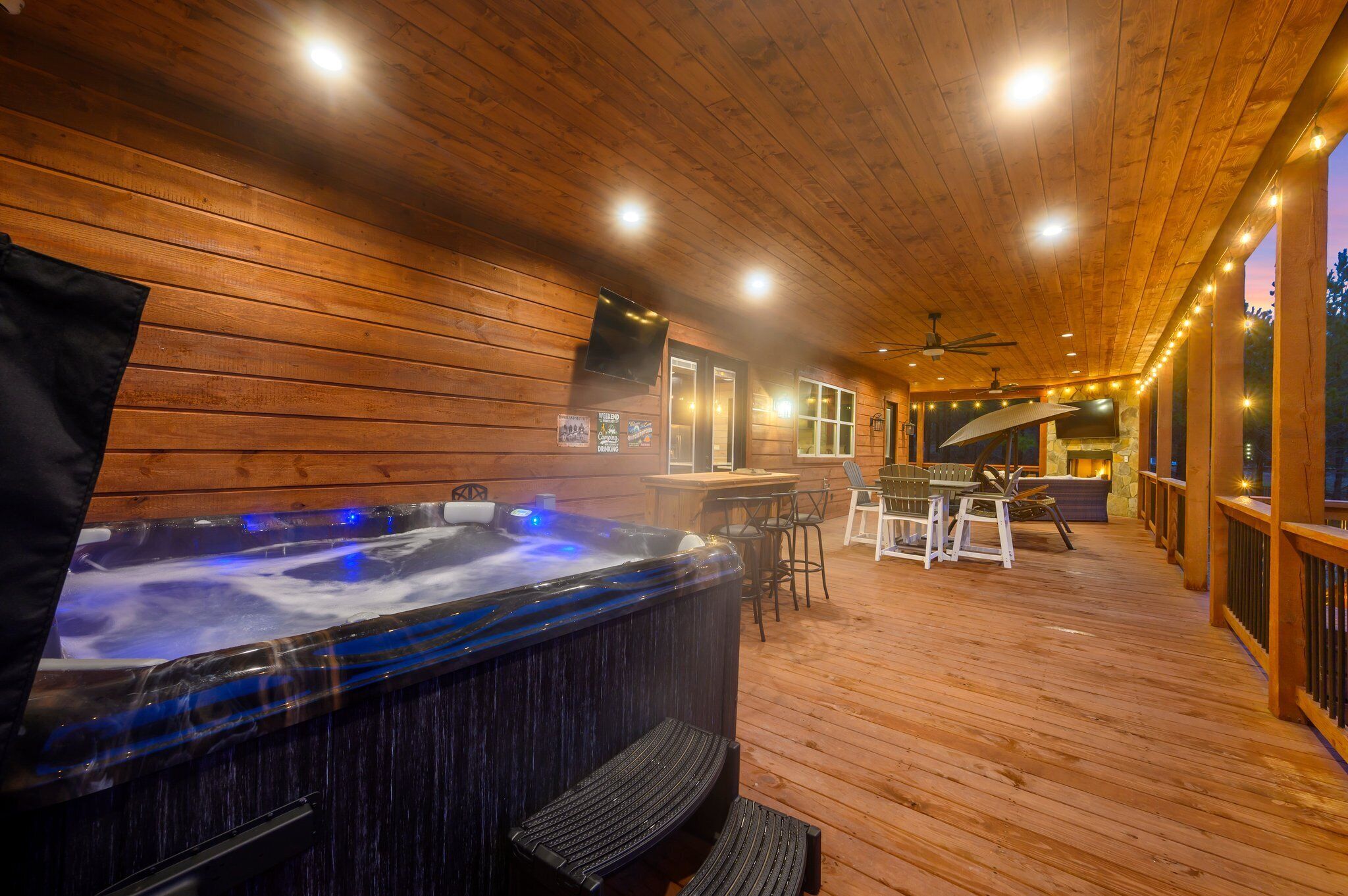Una terraza de madera con jacuzzi, mobiliario exterior y chimenea de piedra.
