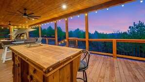 A wooden deck with a bar area, ceiling fans, and string lights.