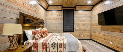 A wooden-paneled bedroom with a bed, nightstand, lamp, and a ceiling fan.