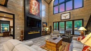 A spacious living room with a fireplace, comfortable seating, and large windows offering views of the outdoors.