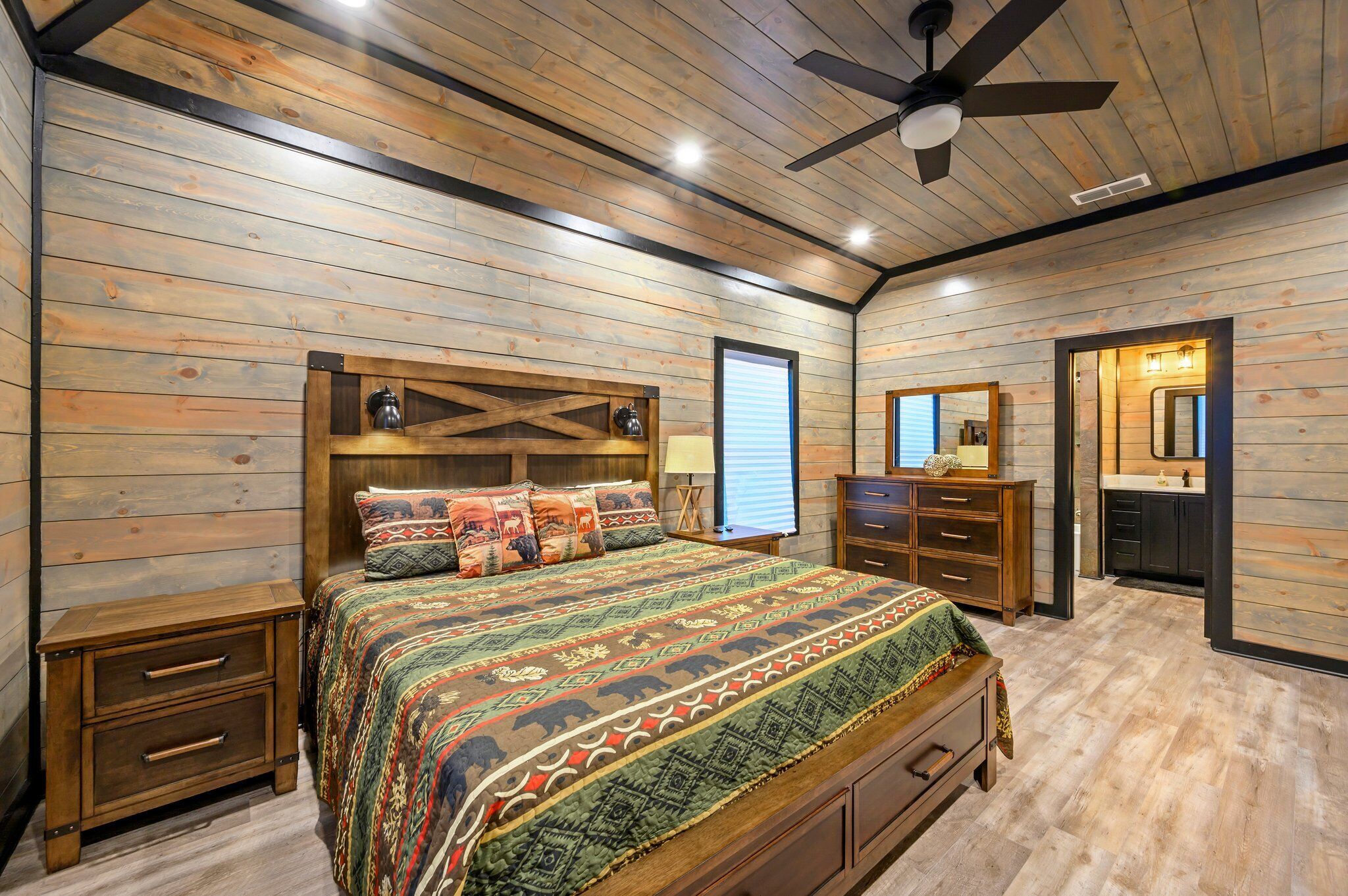 A bedroom with a wooden ceiling, a bed with patterned bedding, a nightstand, a dresser, and a mirror.