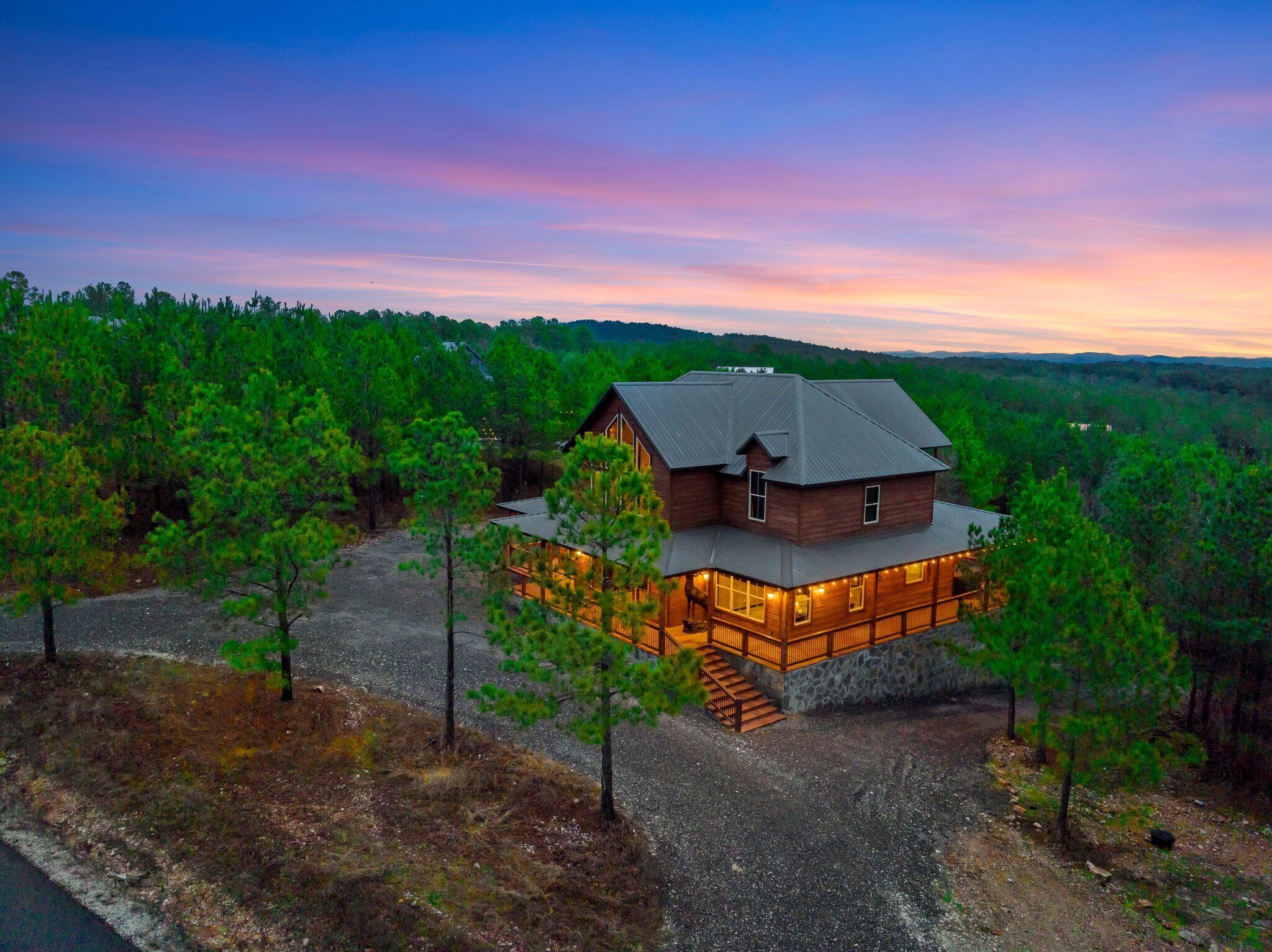 A large, rustic cabin with a stone foundation and a metal roof, surrounded by dense forest.