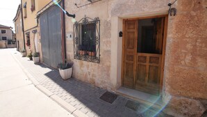 A building with a wooden door, a window with iron bars, and potted plants on the sidewalk.