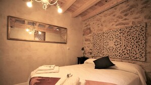 A bedroom with a large bed, a mirror, a decorative wall panel, and a chandelier.