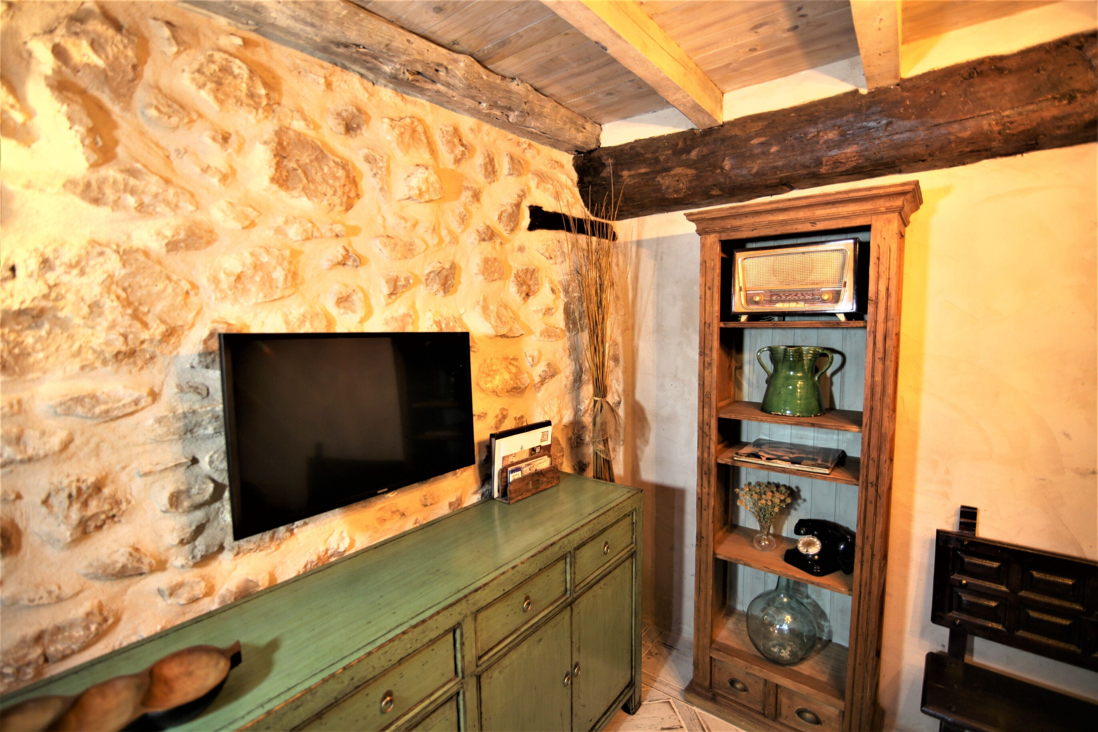 A stone wall with a flat-screen TV mounted on it, wooden shelves with various items, and a green cabinet.