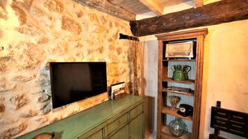 A stone wall with a flat-screen TV mounted on it, wooden shelves with various items, and a green cabinet.