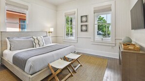 Une chambre à coucher avec un lit, deux fenêtres, une télévision et une petite table.