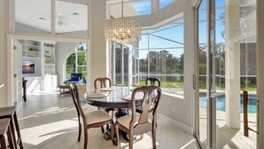 A spacious dining area with a glass table and chairs, a chandelier, and a view of a swimming pool through large windows.