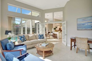 A spacious living area with a sofa, chairs, a coffee table, and a dining area with a kitchen in the background.