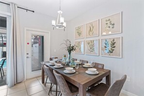 Un comedor con una mesa de madera dispuesta para seis personas, rodeada de sillas, y una araña colgante.