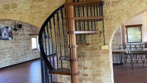 A spiral staircase with a wooden finish and black railings, leading to an upper floor in a room with stone walls and tiled flooring. - Attic Room with Private Bathroom in a Historic Villa Farmstay (Marche)
