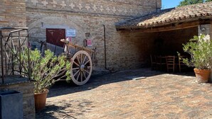 A rustic building with a tiled roof, a wooden cart, and potted plants. - Attic Room with Private Bathroom in a Historic Villa Farmstay (Marche)