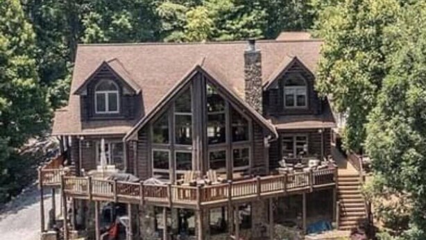 Eine große, zweistöckige Holzhütte mit umlaufender Veranda, umgeben von dichtem Wald.
