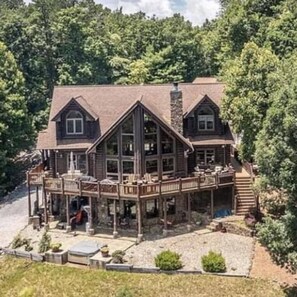 A large, two-story wooden cabin with a wrap-around porch, surrounded by dense forest.
