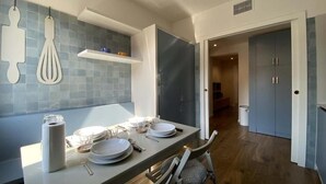 A modern kitchen with a dining area, featuring a white countertop, grey cabinets, and a blue backsplash. - Ca' Magna Apartment  (Venezia)