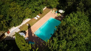 An aerial view of a swimming pool surrounded by lush greenery, with lounge chairs and umbrellas. - Cottage for 4 in a small village near Uzès, with garden, pool and airco (AUBUSSARGUES)