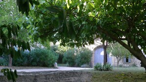 A stone bench in a garden with a stone building in the background. - Cottage for 4 in a small village near Uzès, with garden, pool and airco (AUBUSSARGUES)