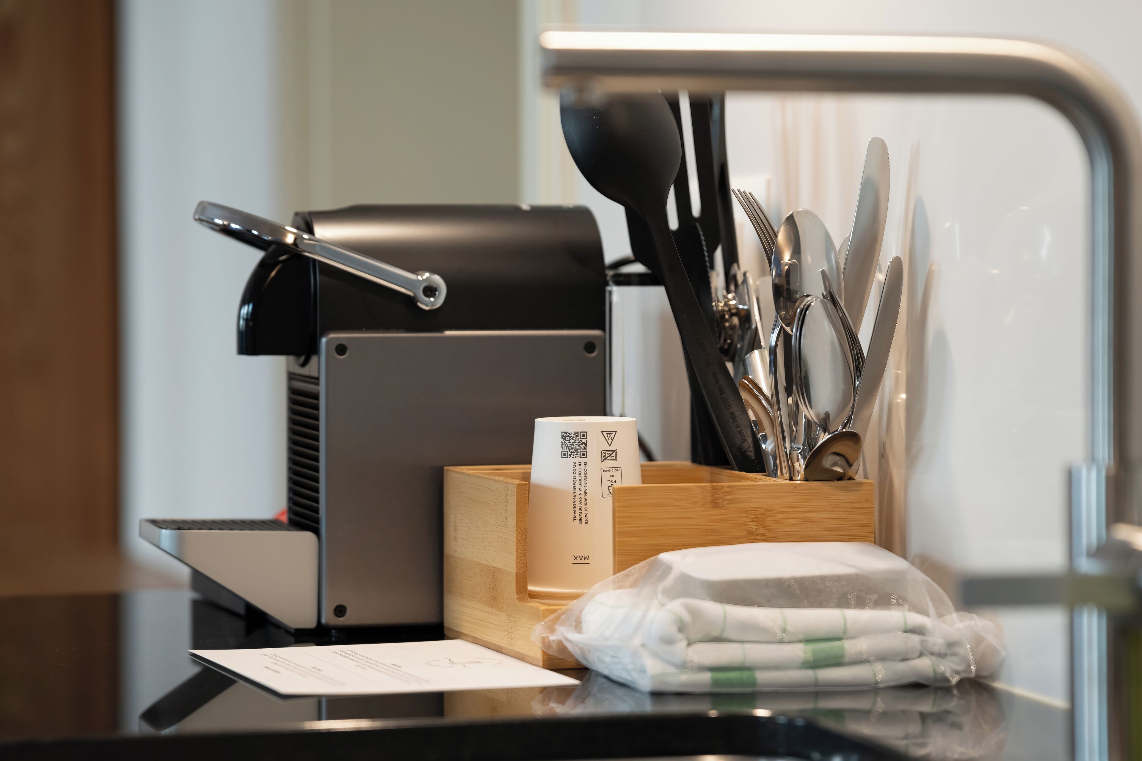 Un coin cuisine équipé d’une machine à café, d’ustensiles, d’un distributeur de serviettes et d’un reçu posé sur le comptoir.