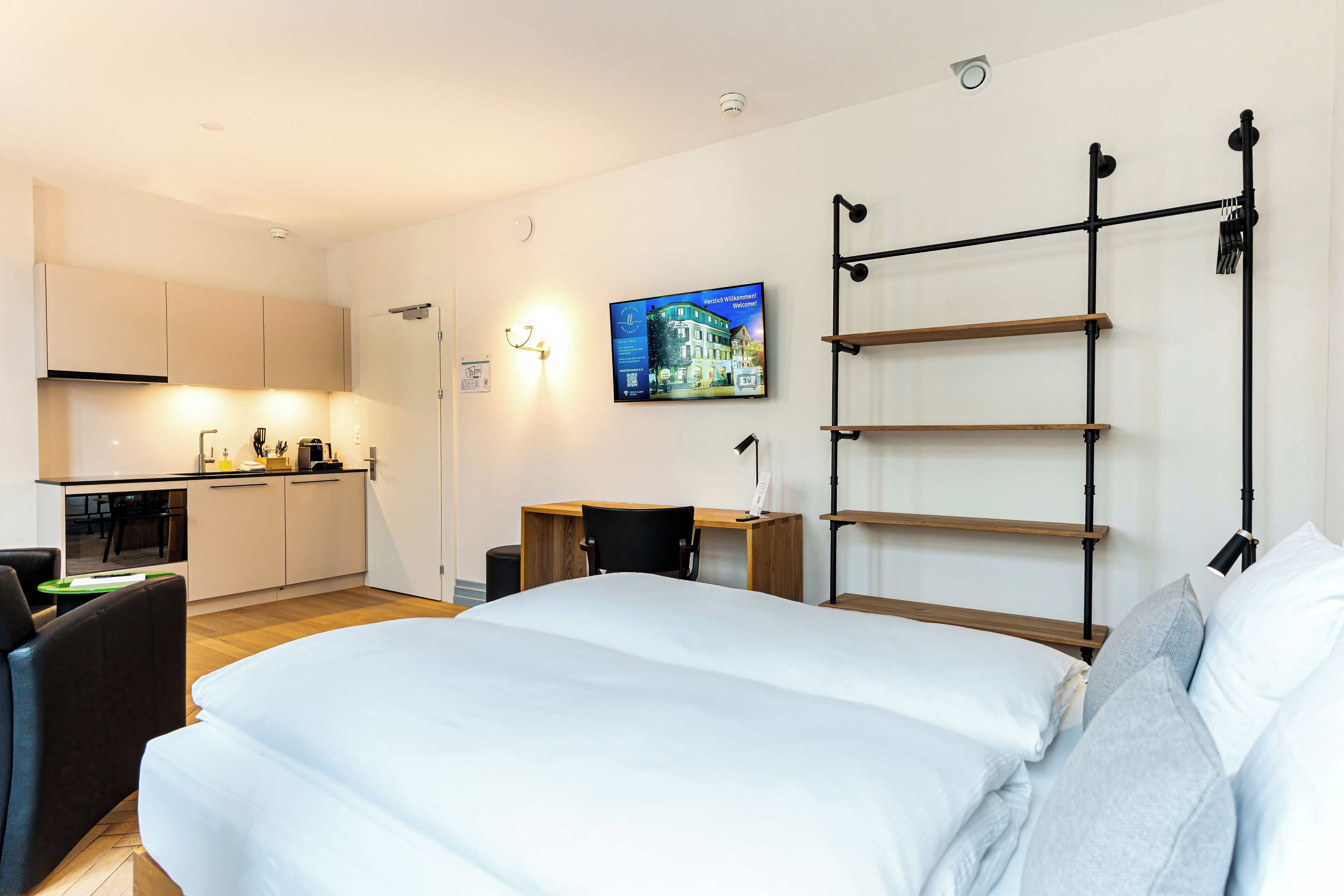 Une chambre d’hôtel moderne équipée d’un lit, d’un bureau, d’une chaise et d’une kitchenette.