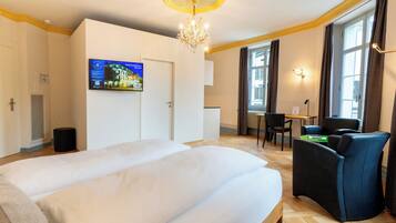 Une chambre d’hôtel avec un grand lit, un bureau avec une chaise, un lustre et un téléviseur fixé au mur.