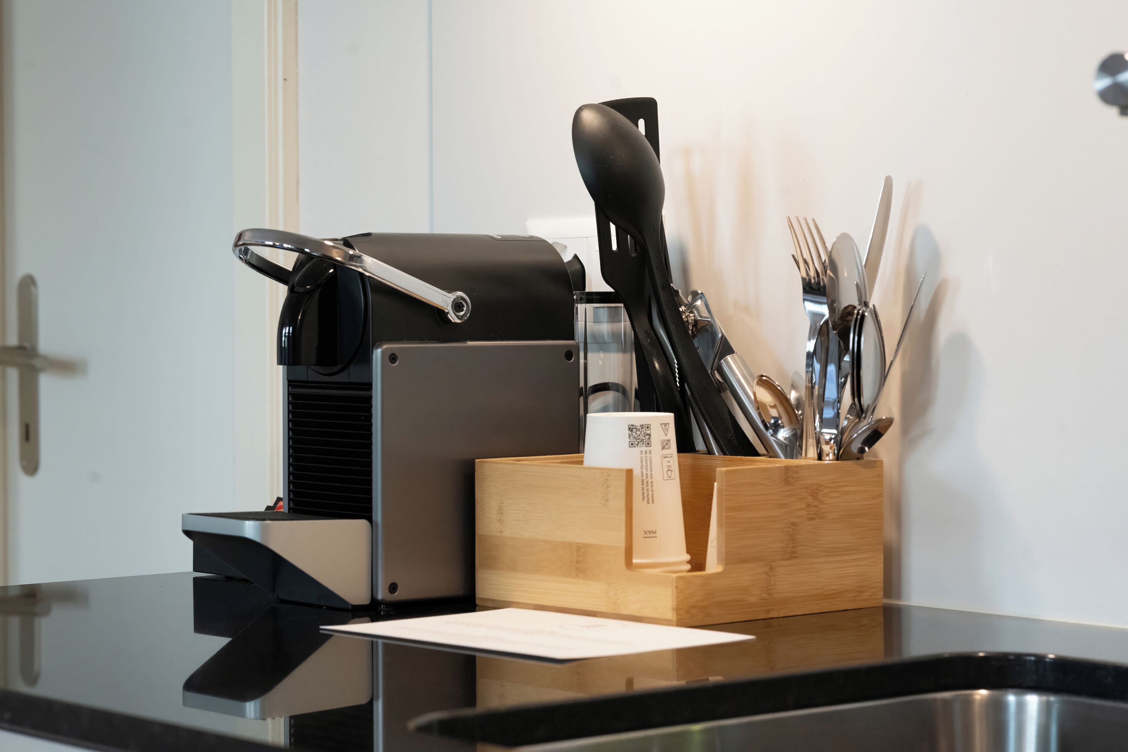 Un plan de travail de cuisine avec une machine à café, un porte-ustensiles en bois et un évier en acier inoxydable.