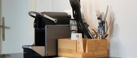 Un plan de travail de cuisine avec une machine à café, un porte-ustensiles en bois et un évier en acier inoxydable.