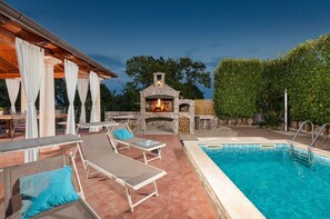 An outdoor pool area with lounge chairs, a stone-built outdoor oven, and a clear blue pool. - Villa Sole by Villsy (Opatija)