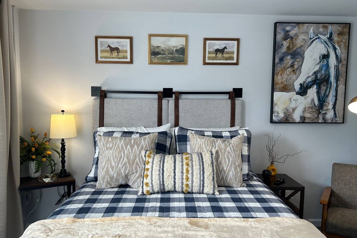 A hotel room with a checkered bedspread, two headboards, three framed horse paintings on the wall, and a large horse painting above the bed.