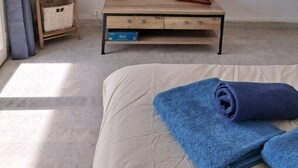 A bedroom with a bed, a TV mounted on the wall, a wooden side table with a router and a book, a shelf with a basket, and a 'HAPPY' sign on the wall. - Agréable Studio Avec Cave et Parking Privatifs (La Ciotat)